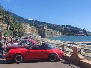 A coastal area with parked vintage cars, a rocky shoreline, and buildings in the background. - Kastegno 8 by Interhome (Rapallo)