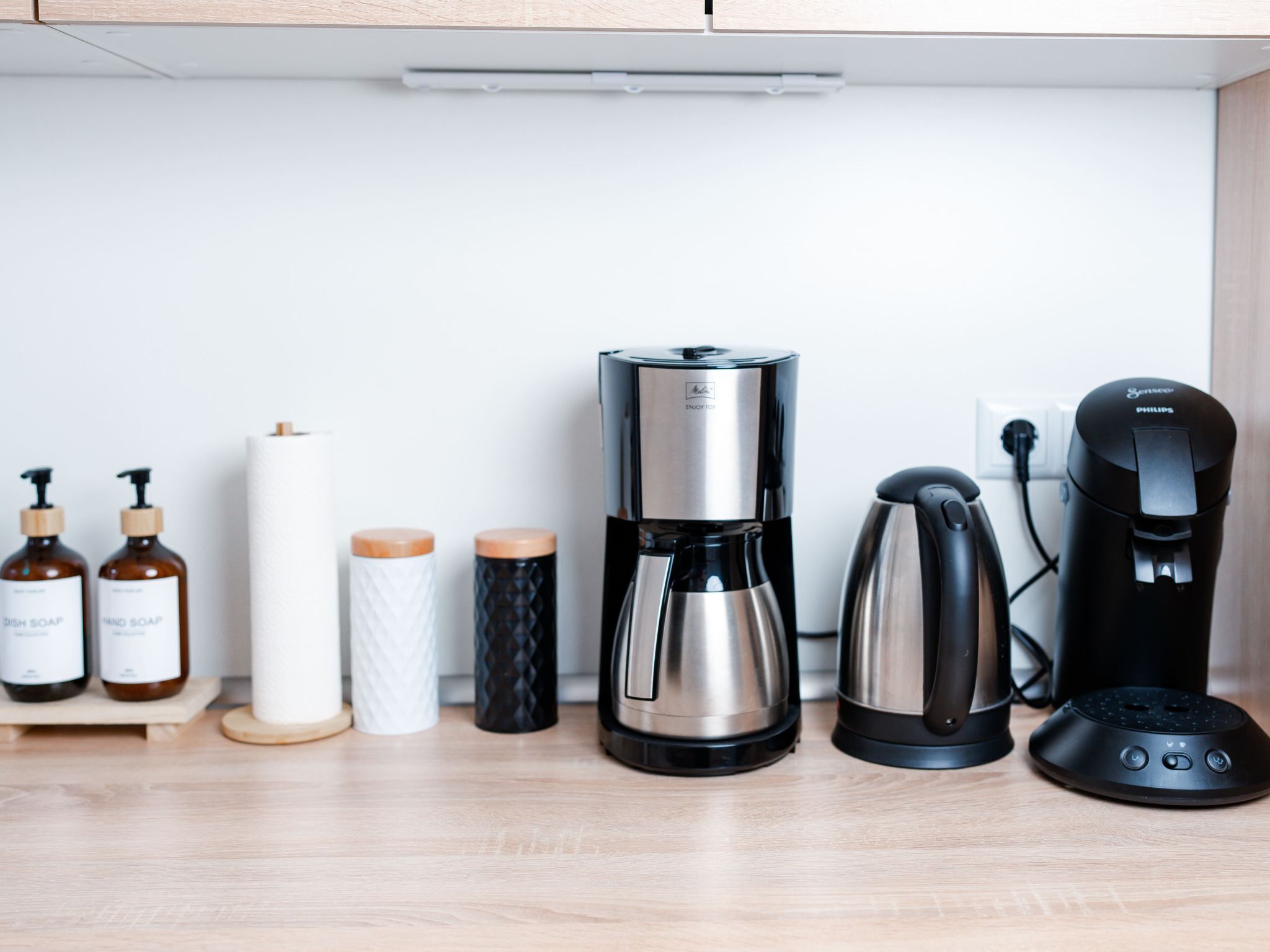 Een keukenblad met een koffiezetapparaat, een waterkoker, een Philips koffiemachine en twee flessen afwasmiddel.