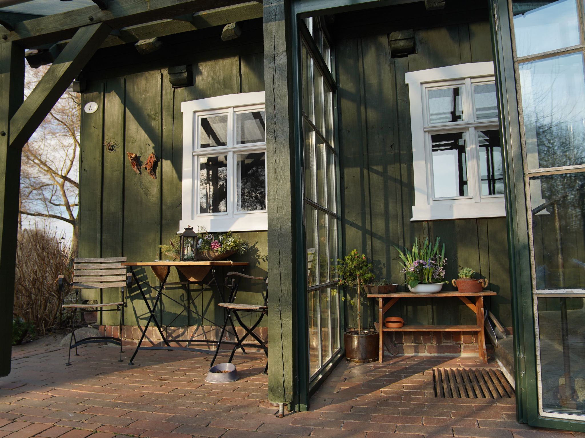 A wooden structure with a bench, a table with potted plants, and a window.