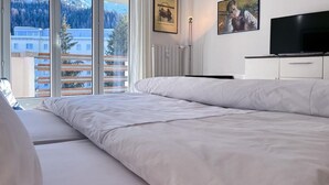 Un dormitorio con una cama grande, televisión y ventana con vistas a edificios y árboles.
