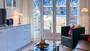 Un salón moderno con una mesa de centro de vidrio, un sofá de cuero y vistas a un paisaje montañoso a través de amplios ventanales correderas.