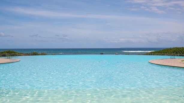 Piscina azul e límpida com vista para o oceano e uma ilha ao longe.
