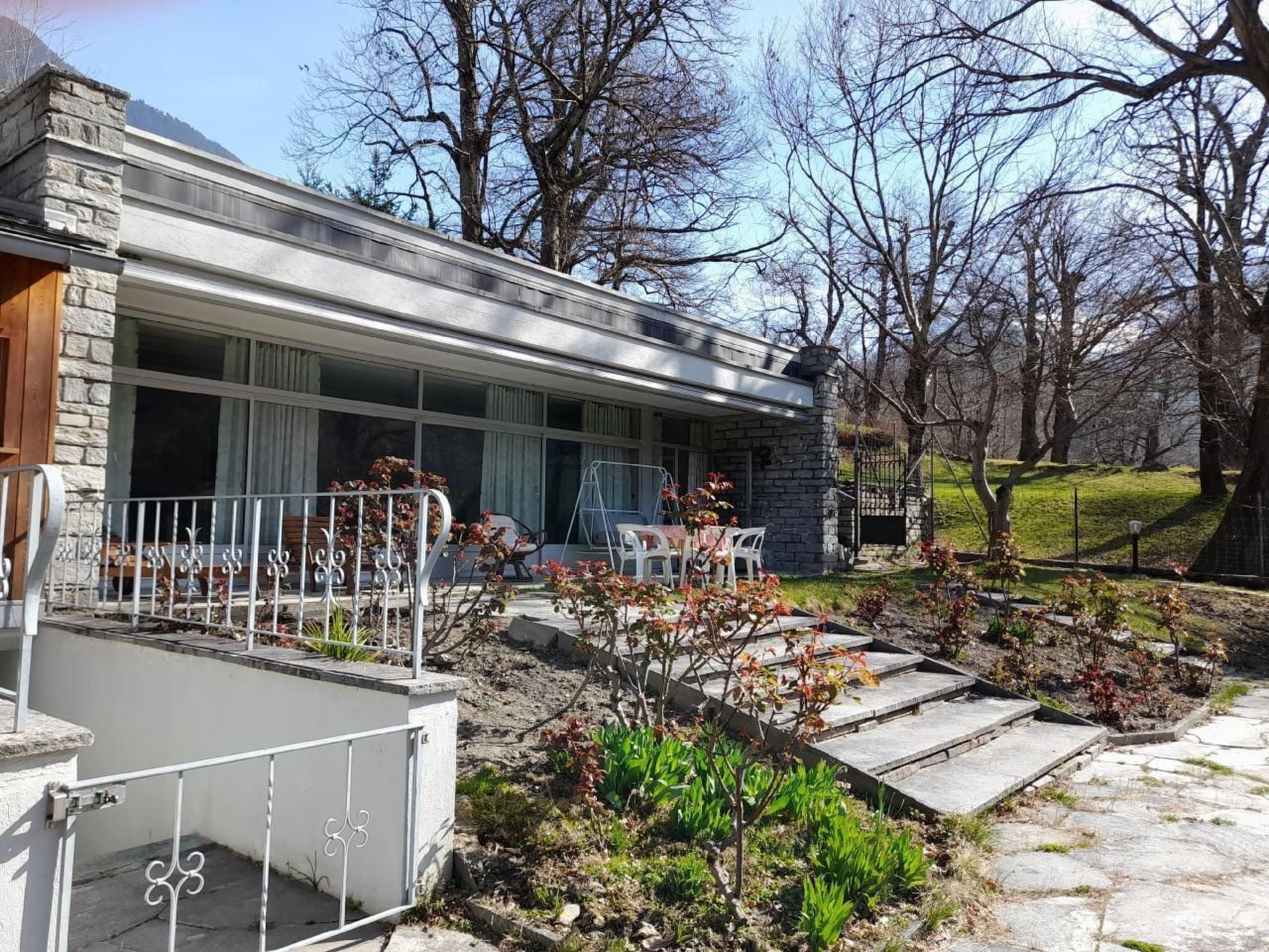 A modern house with a stone facade, large windows, and a patio area with outdoor furniture.