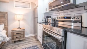 Una cocina compacta con electrodomésticos modernos, una mesita de noche de madera y una cama con cabecero.
