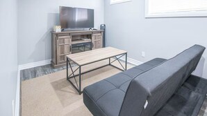 Un espacio habitable compacto con sofá, una mesita de madera, un televisor sobre un mueble y una ventana con persianas.