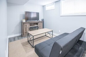 A compact living space with a sofa, a small wooden table, a TV on a cabinet, and a window with blinds. - Adorable Bachelor unit, close to hospitals, shopping centres and downtown Ottawa (Ottawa)