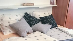 A bed with a star-patterned bedspread and pillows, a wooden headboard, and a shelf above the bed. - Derby 37 by Interhome (St. Moritz)