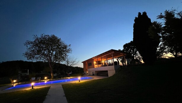 A modern building with a covered patio area, a swimming pool with illuminated edges, and a pathway leading to the building.
