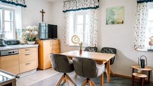 A modern kitchen with a dining area, featuring a wooden table, grey upholstered chairs, and a television on a wooden cabinet.