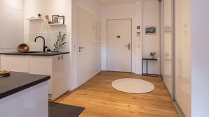 Ett modernt kök med vita skåp, en svart bänkskiva och ett trägolv. På bänkskivan står en liten växt och på golvet ligger en rund matta.