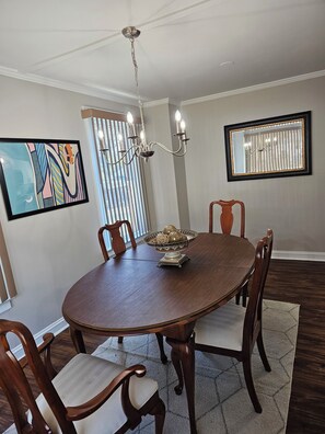 A dining room with a round table, wooden chairs, a chandelier, a mirror, and a painting on the wall. - Furnished Atlanta Home Near Airport & Hospitals - Car Available (Atlanta)