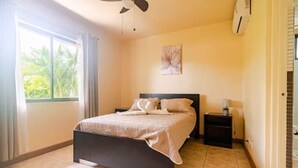 Une chambre à coucher avec un lit, une table de chevet, un ventilateur de plafond et une fenêtre avec des rideaux.
