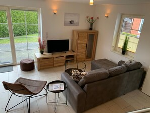 Ein modernes Wohnzimmer mit grauem Sofa, einem Holzkabinett, einem Fernseher und einem Glastisch.