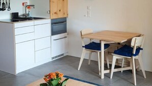 A modern kitchen with wooden cabinets, a built-in oven, and a dining area with a wooden table and two chairs. - Rosatsch B15 - Champfèr by Interhome (St. Moritz)