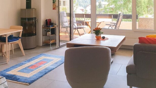 A modern living room with a sofa, a coffee table, and a dining area with a table and chairs. There is a sliding glass door leading to an outdoor patio area. - Rosatsch B15 - Champfèr by Interhome (St. Moritz)