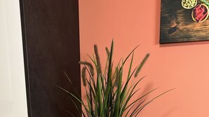 Ein weißer Pflanzkasten mit einer hohen, grünen Pflanze auf Holzboden, neben einem weißen Schrank und einem grauen Stuhl, mit einer pfirsichfarbenen Wand und einem Gemälde im Hintergrund.