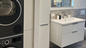 Eine moderne Küche mit eingebauter Waschmaschine und Trockner, einem großen Spiegel über dem Spülbecken und einer Arbeitsplatte mit Seifenspender.