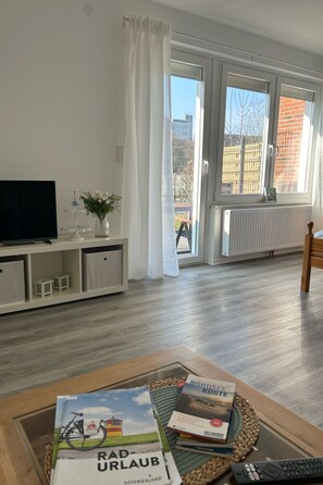 Ein Wohnzimmer mit Fernseher, Büchern und Blick auf eine Stadtkulisse durch große Fenster.