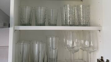 Ein weißes Schrank mit Regalen, auf denen verschiedene Gläser, darunter Tumbler und Weingläser, stehen.
