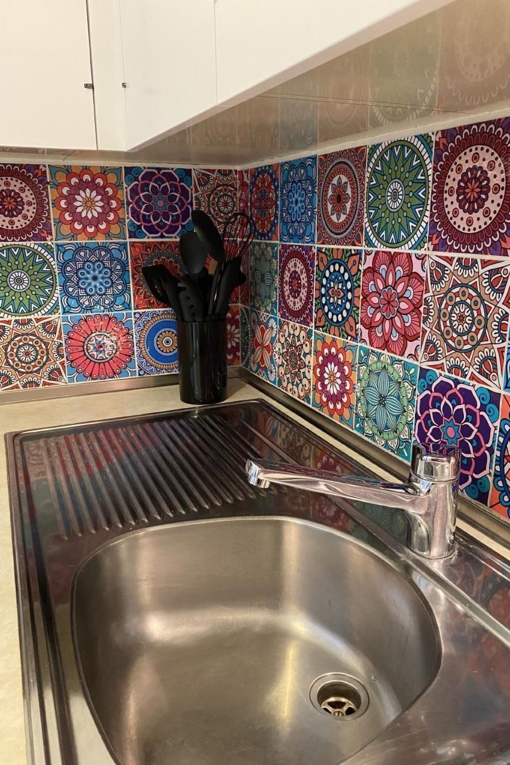 Een keuken met een roestvrijstalen spoelbak, kleurrijke, patroon-tegels op de achterwand en een zwarte pannenhouder.