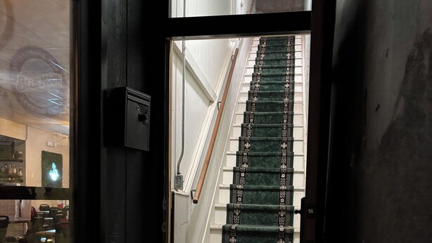 A staircase with green carpet leading to a room with a white door and a window. - Cattlemen’s Quarters 3 Bed 2 Bath Apartment (Hebron)