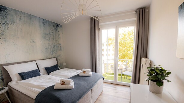 Ett modernt hotellrum med en stor säng, ett skrivbord och en balkong med utsikt över staden.