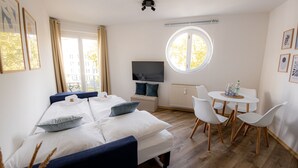 Ett modernt hotellrum med en stor säng, en tv, ett litet matbord och ett runt fönster.