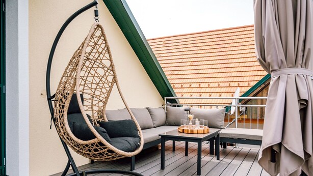 A balcony with a hanging chair, a sofa, and a table with glasses and a tray. - dasWeinbergblick - Landhaus dasThomas by Interhome (Henndorf im Burgenland)