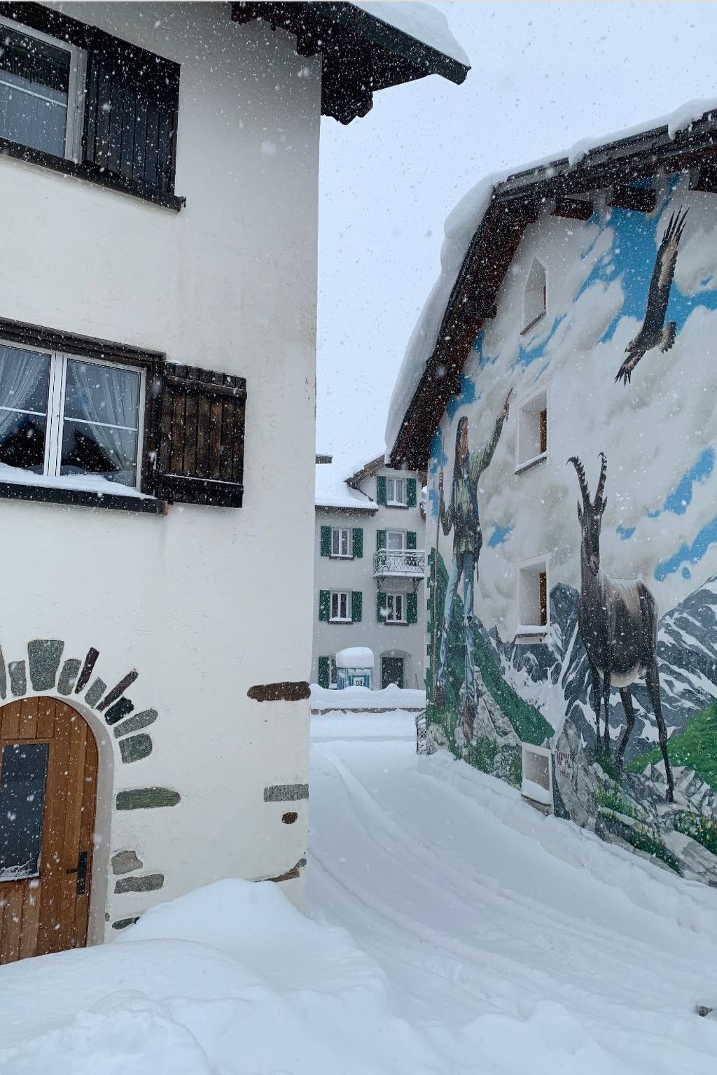 A snow-covered building with a mural of a mountain scene and a wooden door.