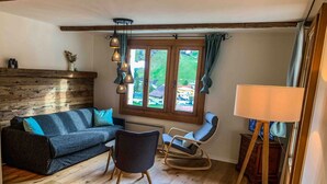 Un salon chaleureux avec un plancher en bois, un canapé bleu foncé, un fauteuil à bascule et une fenêtre avec des rideaux.