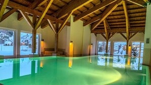 Une piscine intérieure avec des poutres en bois, de grandes fenêtres et une vue sur un paysage enneigé.