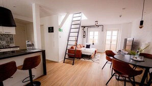 Ett modernt hotellrum med ett litet kök, ett matbord med stolar, en soffa och en trappa.