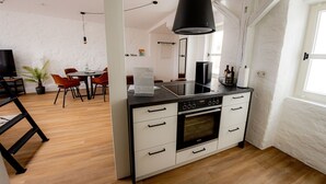 Ett modernt kök med en svart spis, vita skåp och en matplats med trästolar och ett bord.