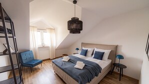 Un dormitorio con cama, una silla, un escritorio y una lámpara colgante.