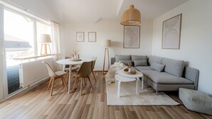 Una sala de estar moderna con un sofá gris, una mesa de comedor redonda y un ventanal grande.