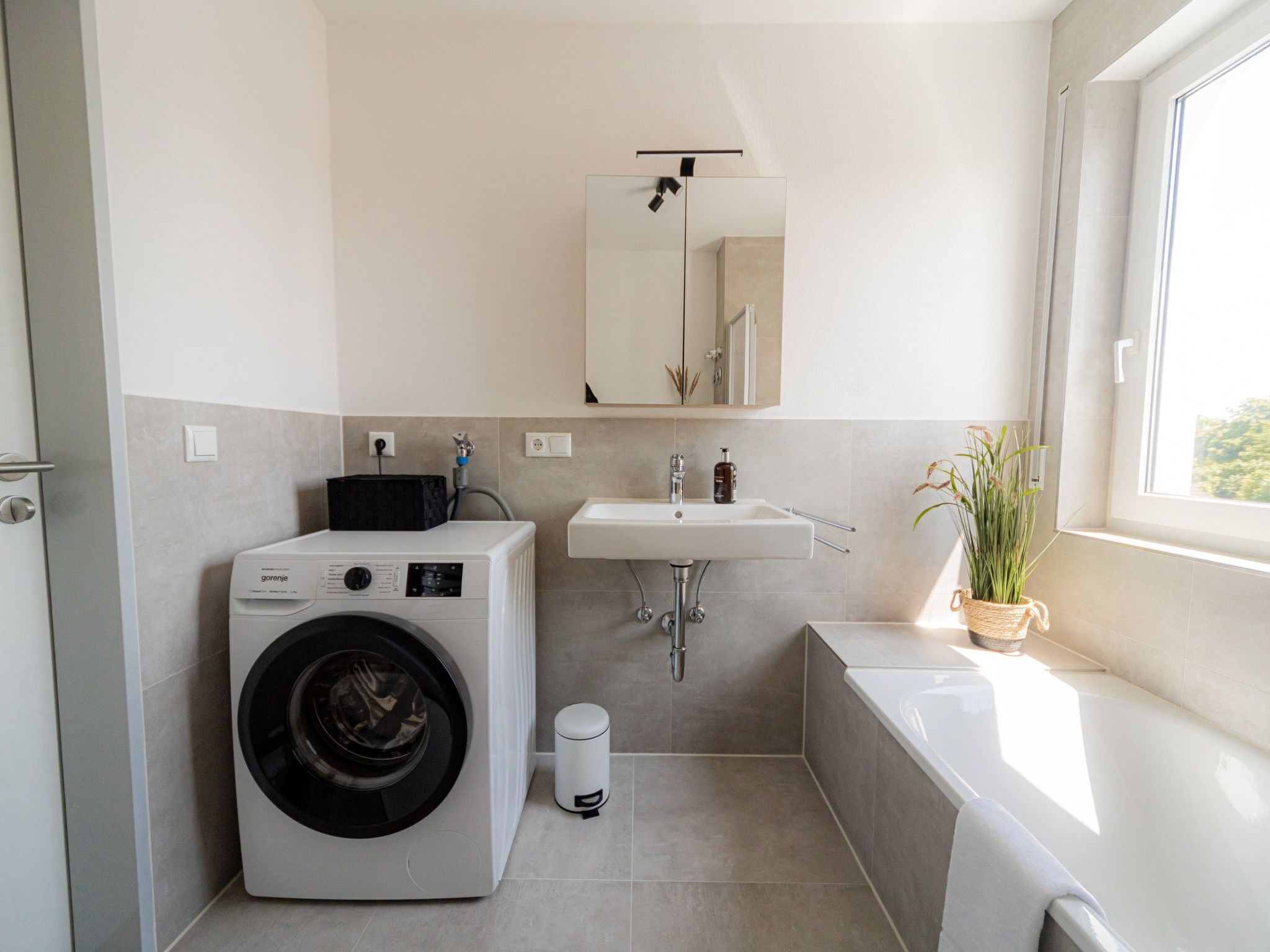 Un baño moderno con lavadora, lavamanos y un ventanal grande.