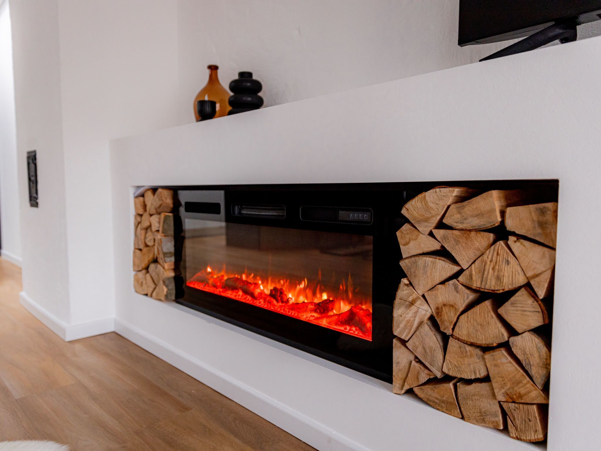 A modern fireplace with a glass front, a log storage area on the right, and a flat-screen TV mounted above it.