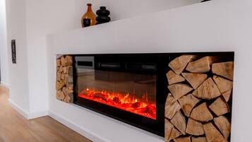 A modern fireplace with a glass front, a log storage area on the right, and a flat-screen TV mounted above it.