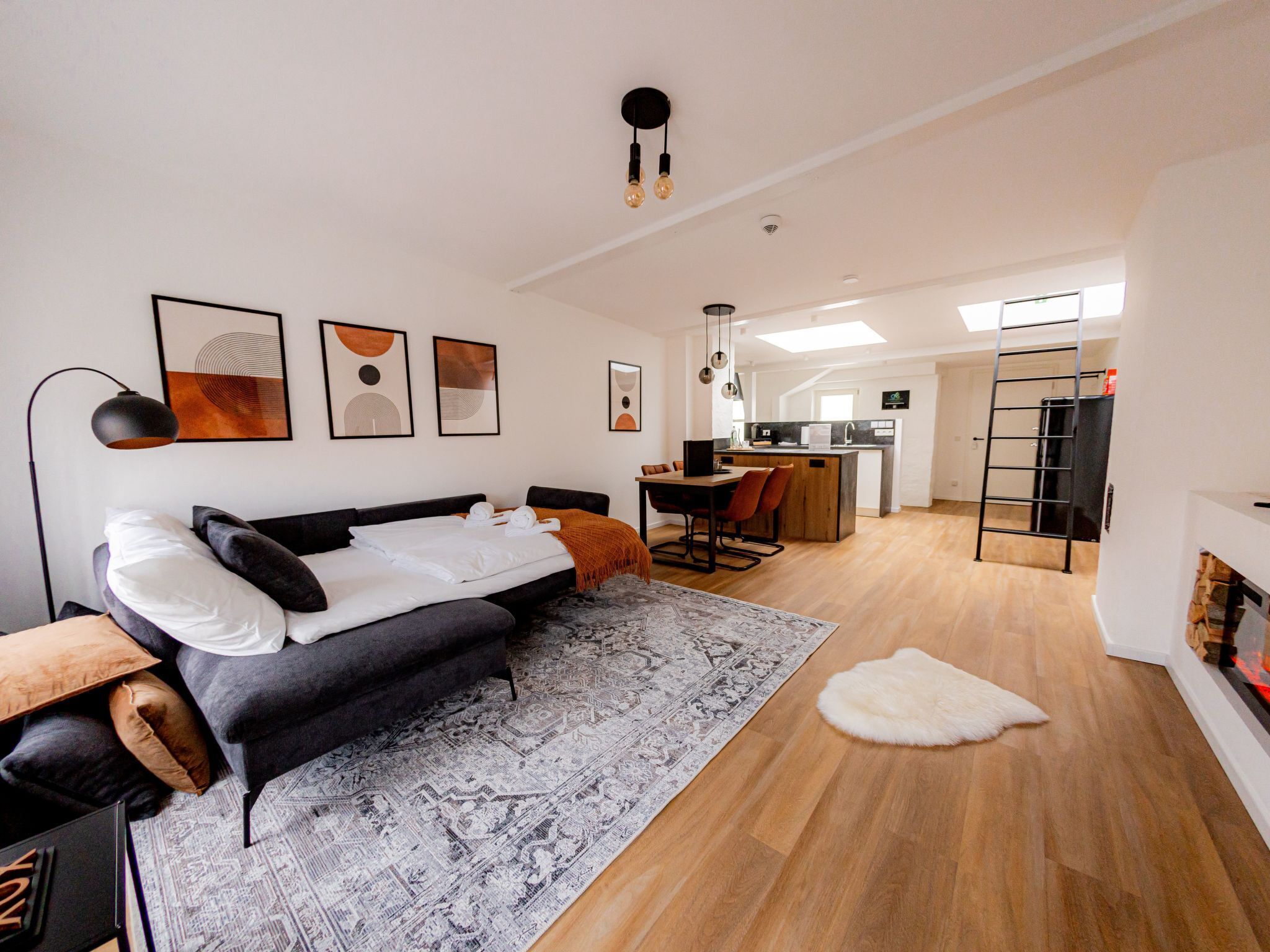 A modern hotel room with a bed, a desk, a kitchen area, and a staircase.