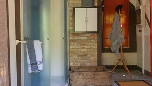 Una stanza con una porta doccia in vetro, un armadietto in legno, un muro in mattoni e uno sgabello di legno.