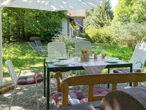 Ein Essbereich im Freien mit einem Tisch für zwei Personen, umgeben von Stühlen und mit Blick auf ein Haus im Hintergrund.
