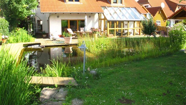 Ett hus med en damm, en terrass och en trädgård.