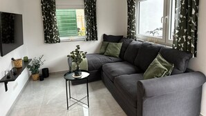Un saló modern amb un sofà gris, una taula rodona petita i un televisor fixat a la paret.