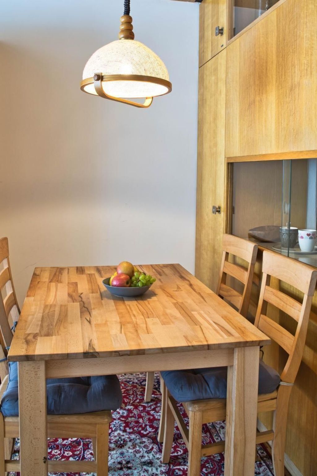A wooden dining table with a bowl of fruit, surrounded by chairs with cushions.