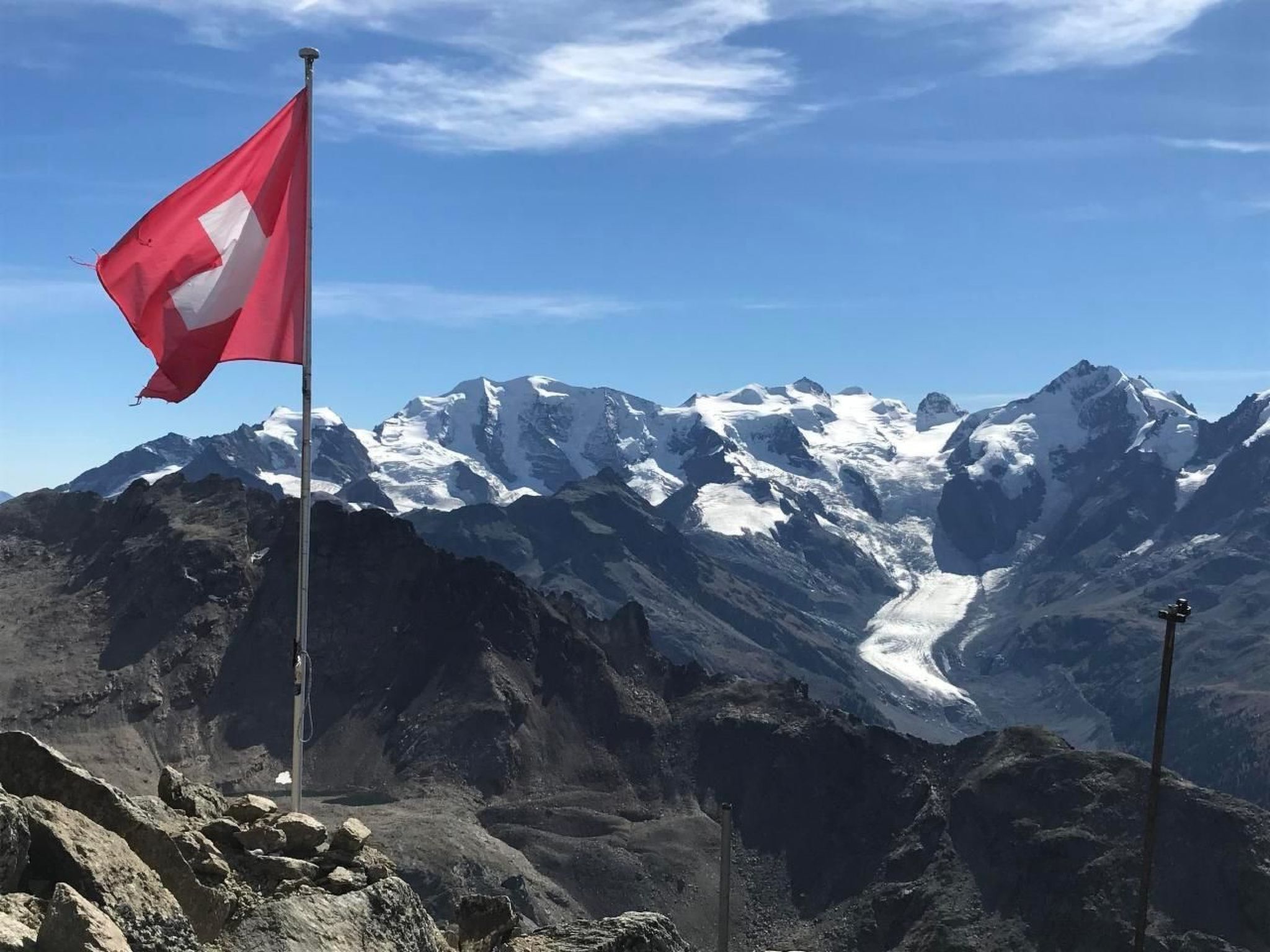 Un drapeau flottant au sommet d’un mât, avec une chaîne de montagnes en arrière-plan.