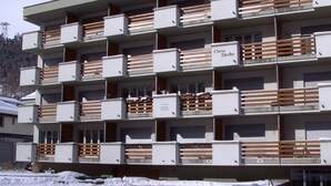 Monikerroksinen hotelli, jossa on parvekkeet, ja sen yläpuolella on kyltti, jossa lukee ”Chesa Derby”, ja maa on lumen peitossa.