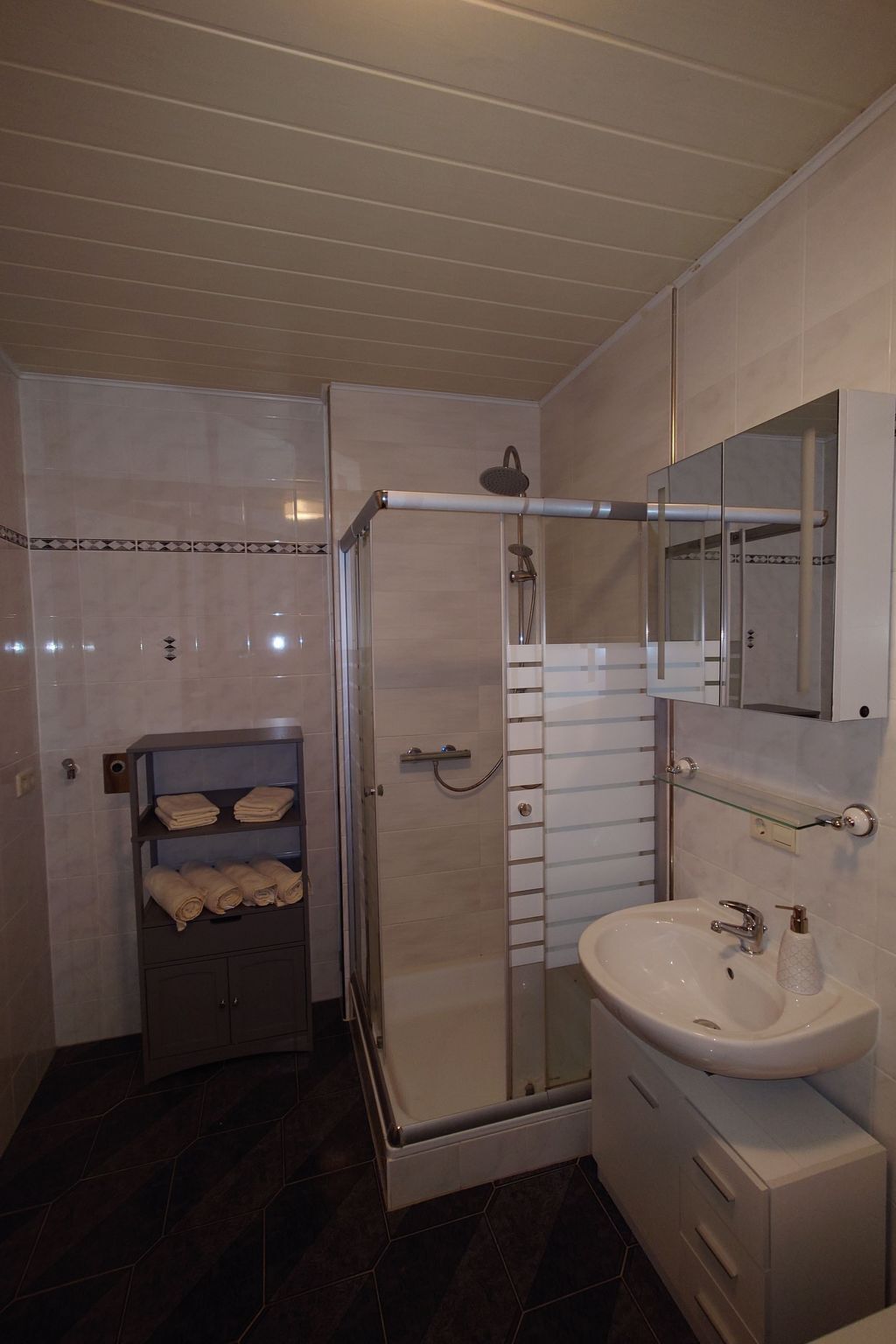 A modern bathroom with a glass-enclosed shower, a white sink with a mirror above it, and a towel rack with folded towels.