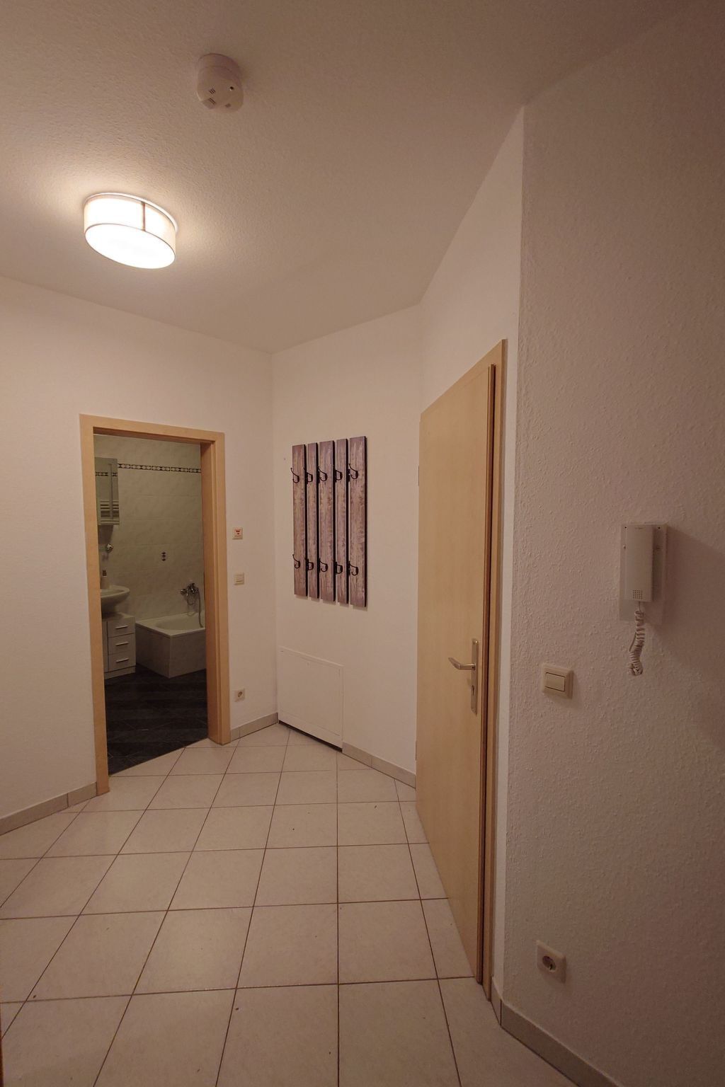 Ein Flur mit gefliestem Boden, einer Tür rechts, einer Wandleuchte und einem Wandtelefon.