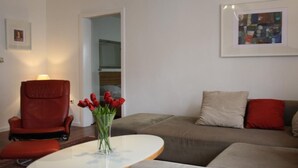 Ett vardagsrum med en brun läderfåtölj, en grå soffa och ett vitt soffbord. På soffbordet står en vas med röda blommor.