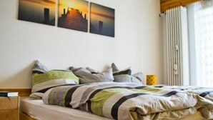 Una camera d'albergo con un letto, un comodino e tre quadri appesi raffiguranti un tramonto su una città.